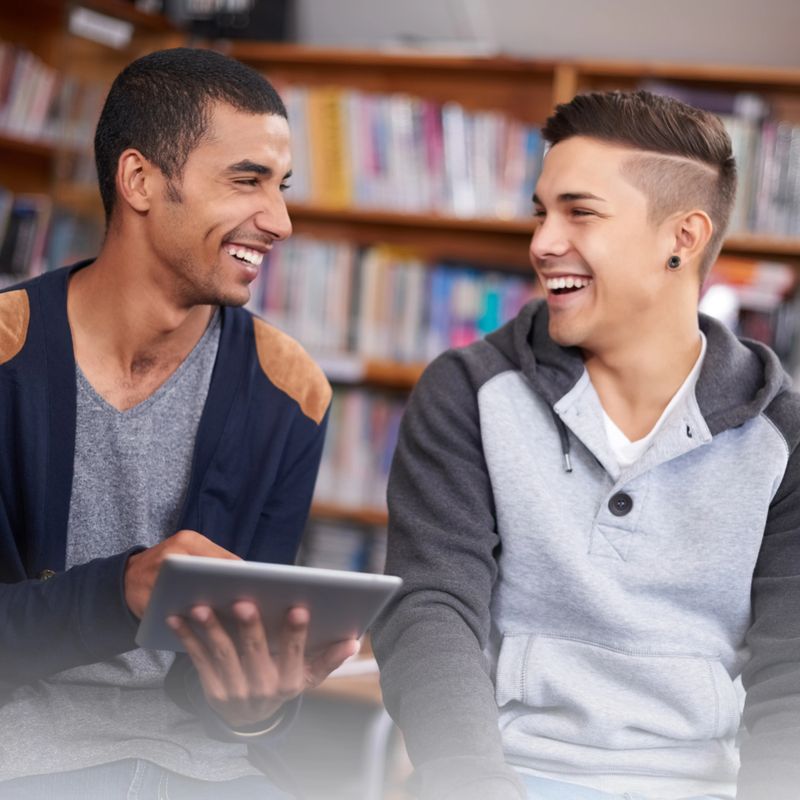 Shot of two young men laughing while using a digital tablet in the university library