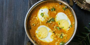 Indian egg curry garnished with cilantro served in a brass bowl.