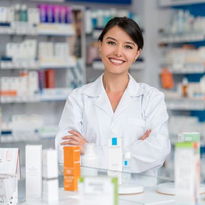 Smiling female pharmacist standing with arms crossed in pharmacy.