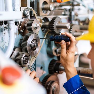 Worker in yellow helmet repairing machinery gears with a screwdriver.