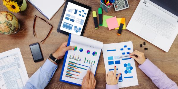Two people analyzing charts and graphs at a wooden desk with office supplies.