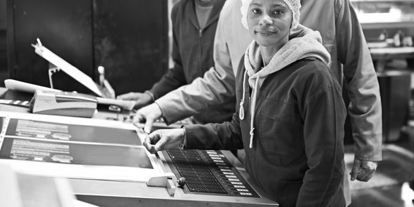 Three diverse factory workers operating printing machinery with safety gear.