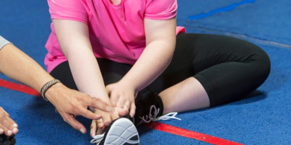 Child stretching legs on gym floor with help.