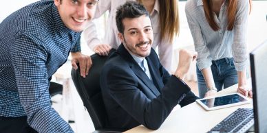Four young professionals smiling around a desk with digital tablets and a computer.