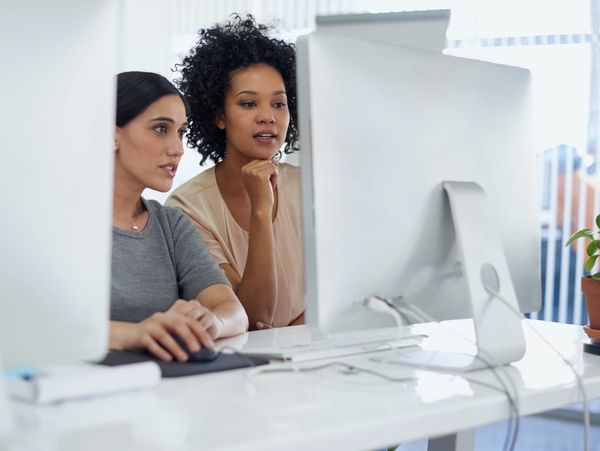 Two women collaborating on a computer in a bright office.