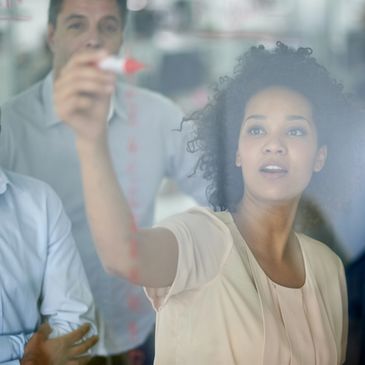 Woman writing on a transparent board while colleagues observe.