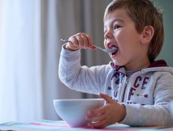 Young boy enjoying a meal with a spoon from a white bowl.
