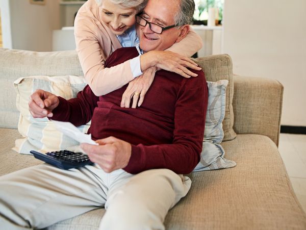 Elderly couple sharing a warm embrace on a couch while reviewing documents.