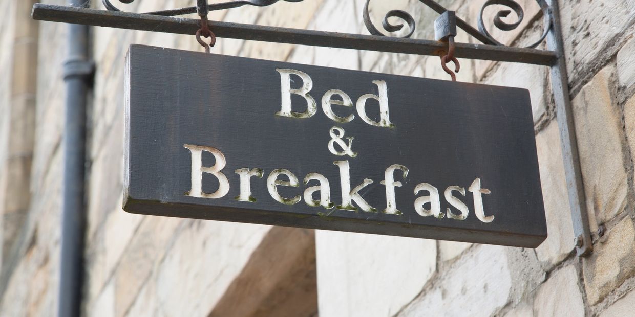 Rustic wooden Bed &amp; Breakfast sign on a stone wall.
