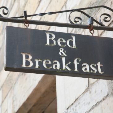 Rustic bed and breakfast sign hanging outside a stone building.