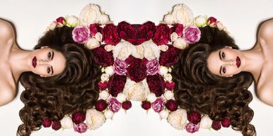 Symmetrical portrait of a woman with dark hair surrounded by colorful flowers.