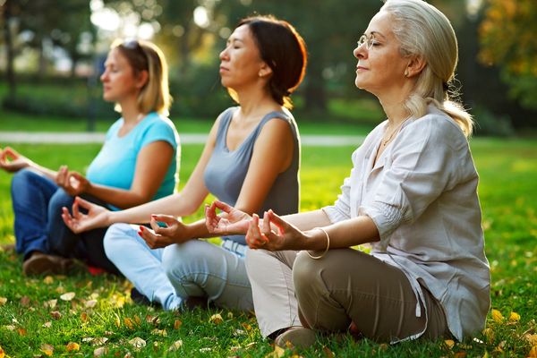 Three women meditating peacefully outdoors on green grass.