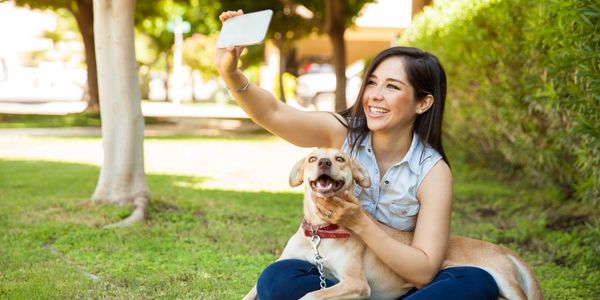 Woman happily taking a selfie with her dog in the park.