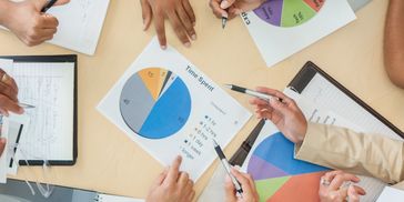 Team collaborating over colorful pie charts and notes in a business meeting.