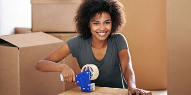Smiling woman packing a box with tape among moving boxes.