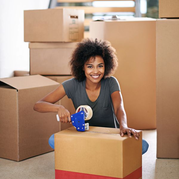 Smiling woman packing a box with tape among moving boxes.