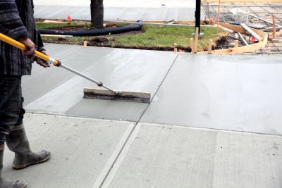 Worker smoothing freshly poured concrete with a tool.