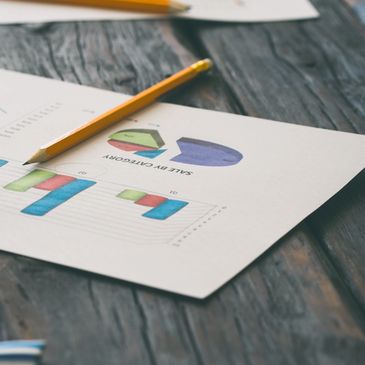 Pencil on a sales report with colorful charts on a wooden table.