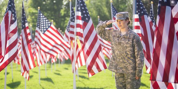Female soldier saluting among American flags on a sunny day.