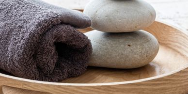 Rolled towel and stacked stones on a wooden tray for spa relaxation.