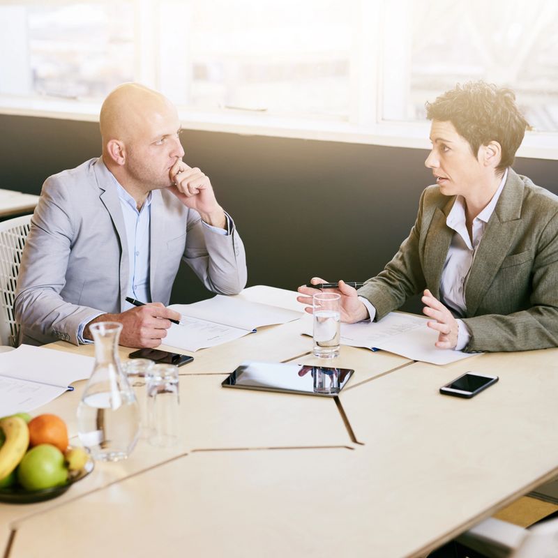 Businesswoman busy explaining her vision for her business to her male business partner while seated at the board room table.