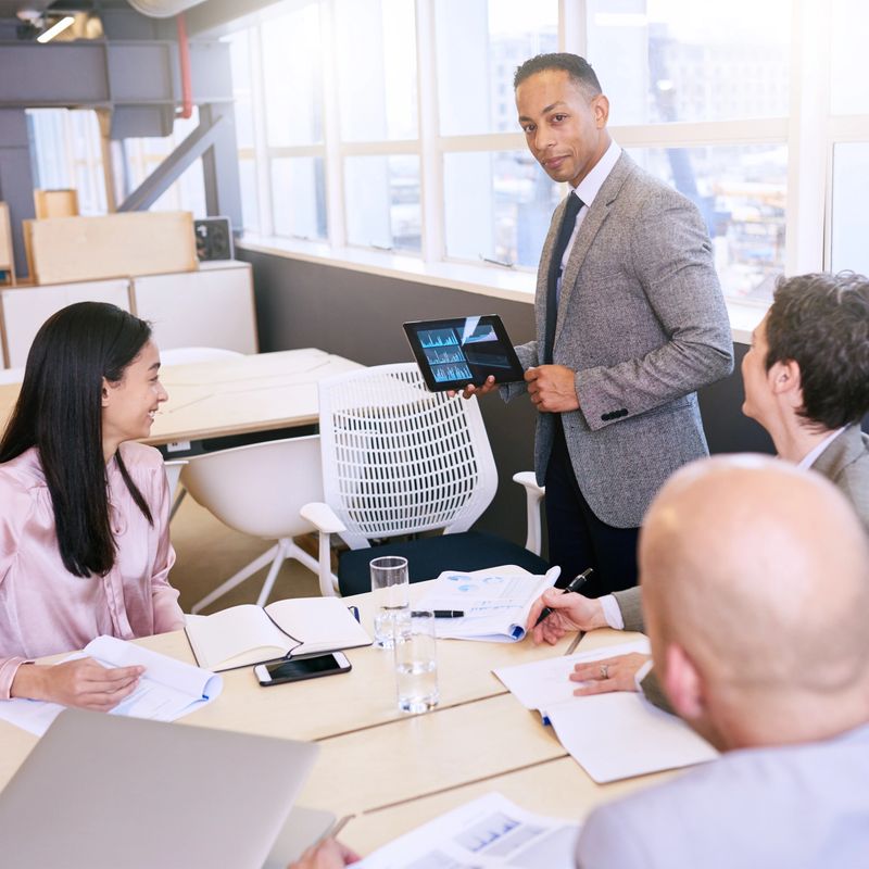 Professional mature adult mixed race well dressed businessman conducting a presentation in a bright modern conference room while holding and using a tablet in his presentation.