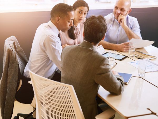 Four professionals engaged in a discussion around a meeting table with documents and tablets.
