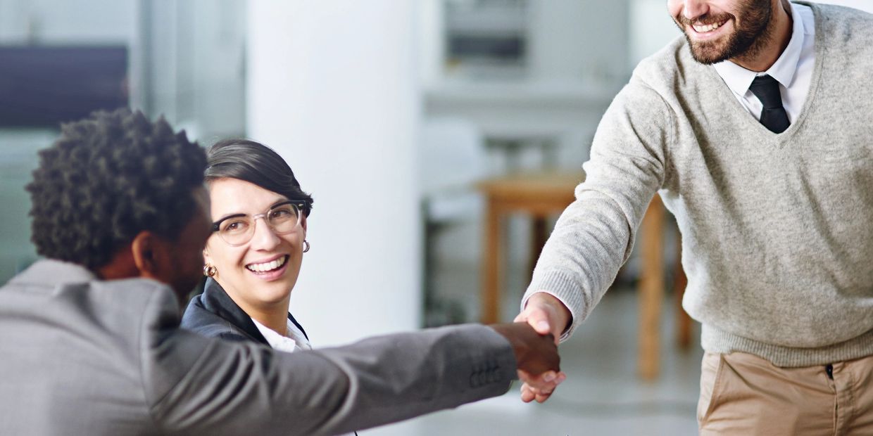 Two men shaking hands while a woman smiles during a business meeting.