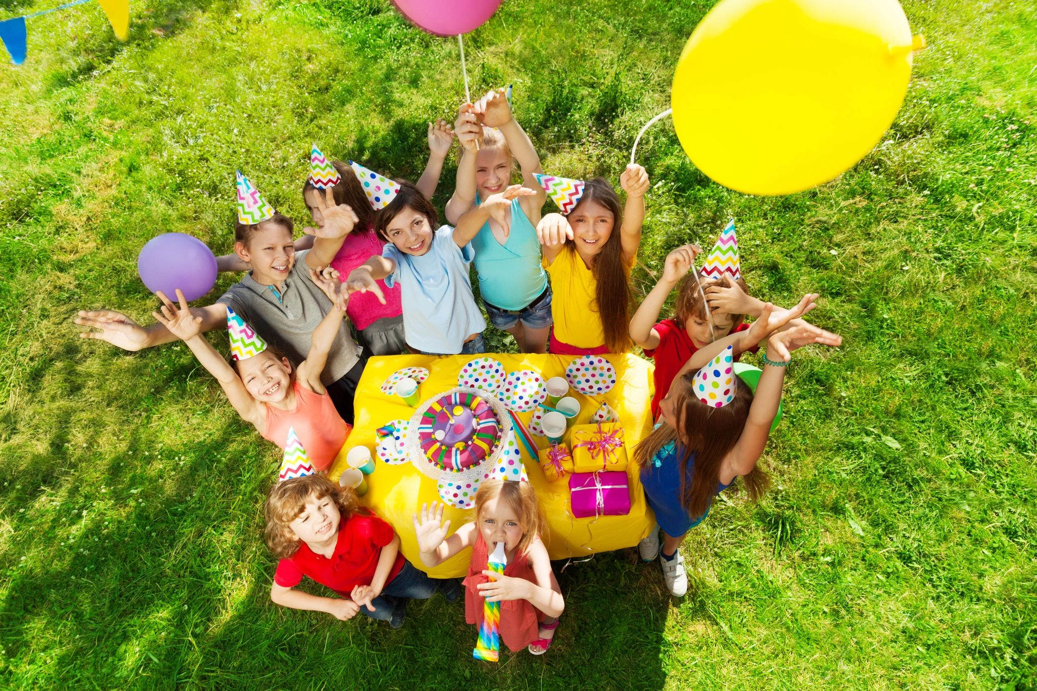 Children celebrating with balloons and party hats at a birthday party.