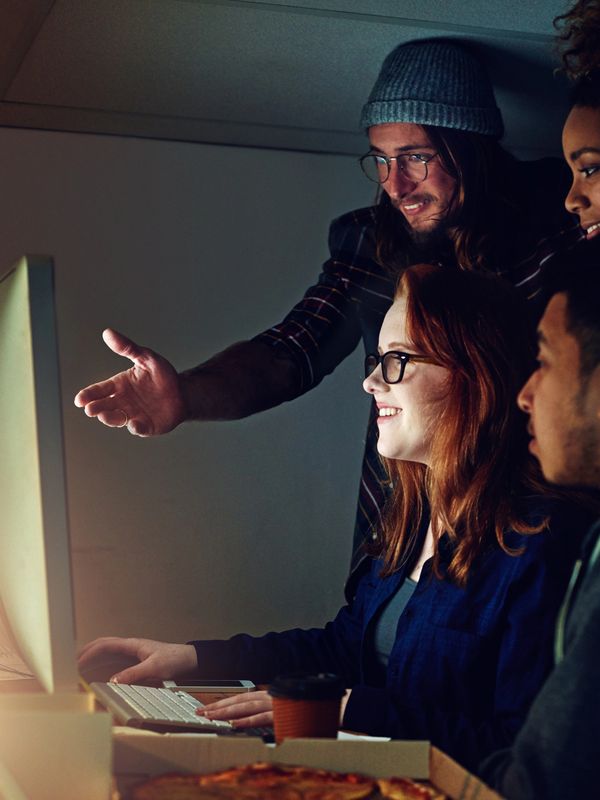 A group of young adults happily collaborating around a computer screen.