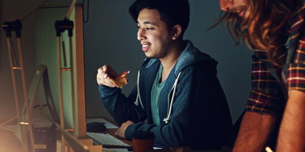 Man eating pizza while working at a computer.
