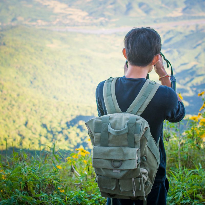 Young traveler standing on big cliff in the mountains and looks into the distance at sunset.