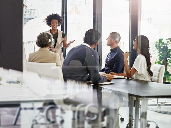 A woman leads a discussion in a modern office meeting with attentive colleagues.