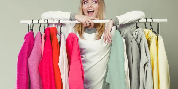 A woman happily posing behind a colorful clothing rack.