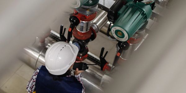 Engineer inspecting industrial pipes and valves using a walkie-talkie.