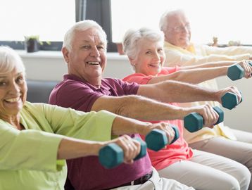 A group of seniors working out, holding dumbells in their hands, while sitting in a chair.