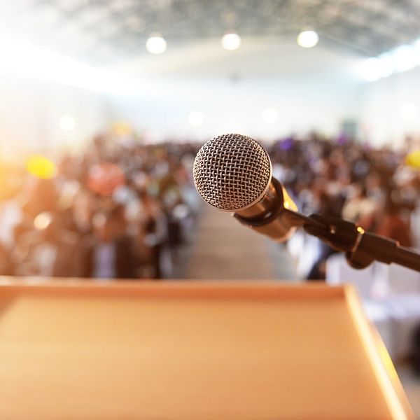 Close-up of a microphone on a podium with a blurred audience in the background.