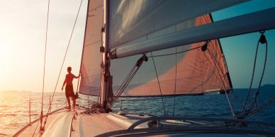 Person standing on a sailboat at sunset, enjoying the sea breeze.