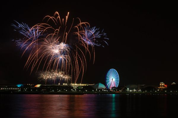 Colorful fireworks over a Ferris wheel at night.