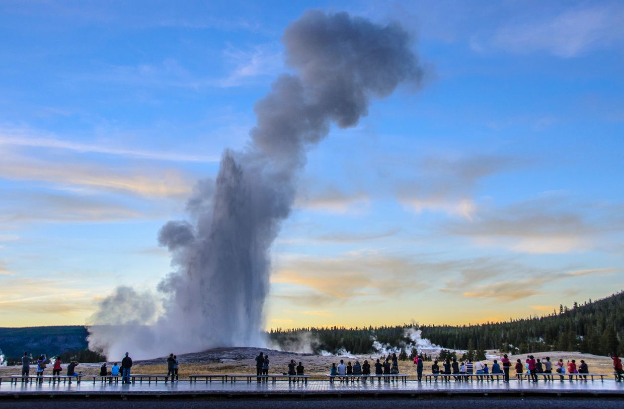 Crowd watching a geyser erupting at sunset in a national park.