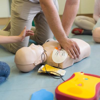 Person performing CPR on a training mannequin with AED nearby.