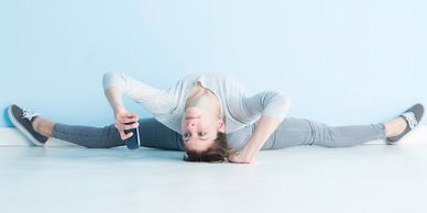 Woman doing the splits while arching her back all the way to the floor and looking at her phone.