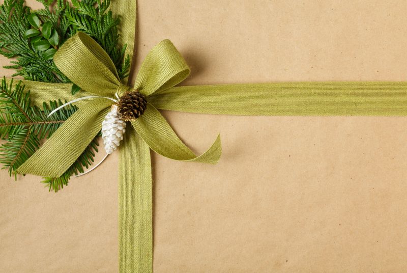 Close up of bow and natural botanical decorations on Christmas gift background. Christmas present wrapped in sustainable recycled wrapping paper with jute bow, pine cones and evergreens.