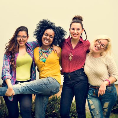 Four diverse women smiling and posing together outdoors.