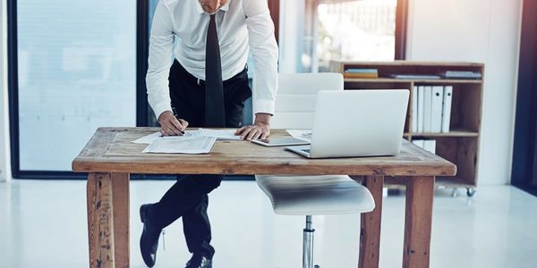 Businessman reviewing documents at a wooden desk with a laptop.