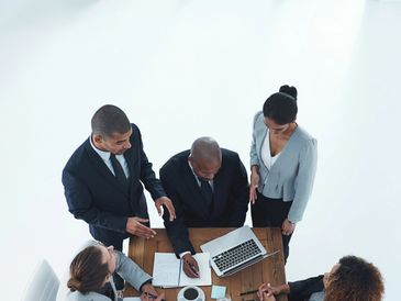 Four professionals collaborating around a table with laptops and documents.