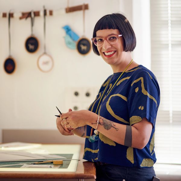 Smiling woman with tattoos holding knitting needles.