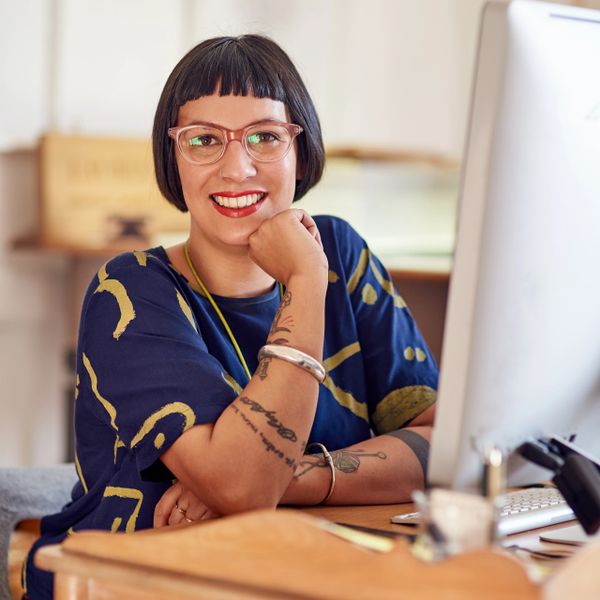 Smiling woman with glasses sitting at a desk in front of a computer.