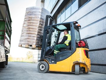 Worker operating forklift to unload materials.