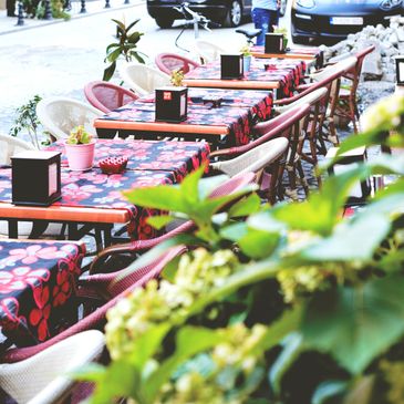 Outdoor café tables with floral tablecloths and chairs along a sidewalk.